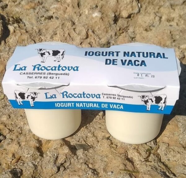 Dos iogurts naturals de llet de vaca amb un blister de cartró que els uneix, amb tons blaus, on hi diu Iogurt natural de vaca i la marca La Rocatova, productors d'aquesta especialitat làctica.